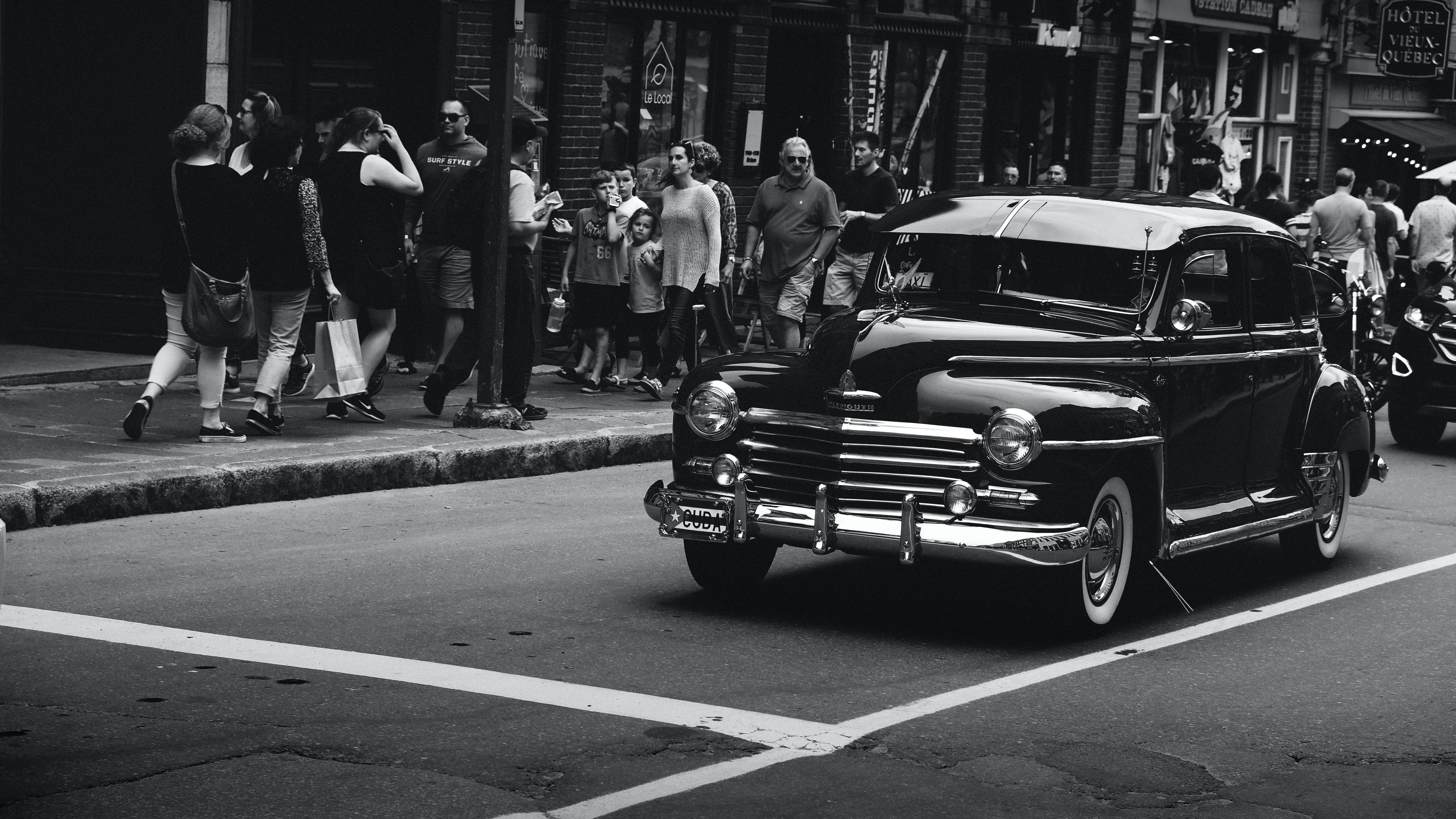 grayscale photography of vehicle on road beside people